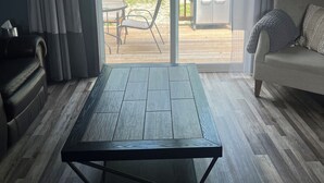 Un saló amb una gran porta corredissa de vidre que dona a un patí exterior, un sofà, una taula de centre i una barbacoa.