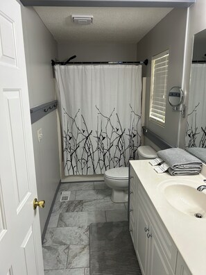A bathroom with a toilet, sink, and shower curtain with a branch pattern. - 3-bedroom house in charming Jackson Springs. Not to far from the course. (Jackson Springs)