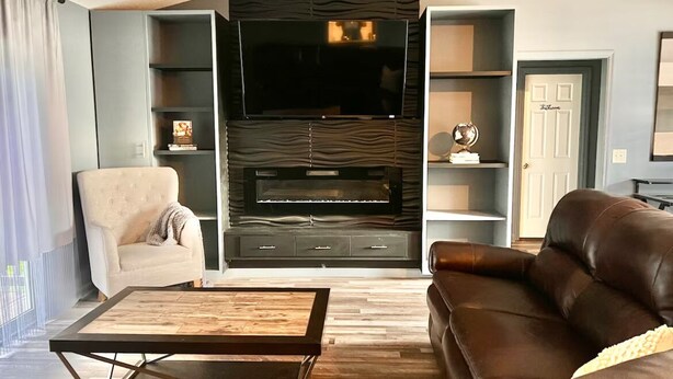 Un saló modern amb un sofà de cuir marró, una taula de centre de fusta, un butac armchair gris i un moble d'entreteniment encastrat amb un televisor de pantalla plana.