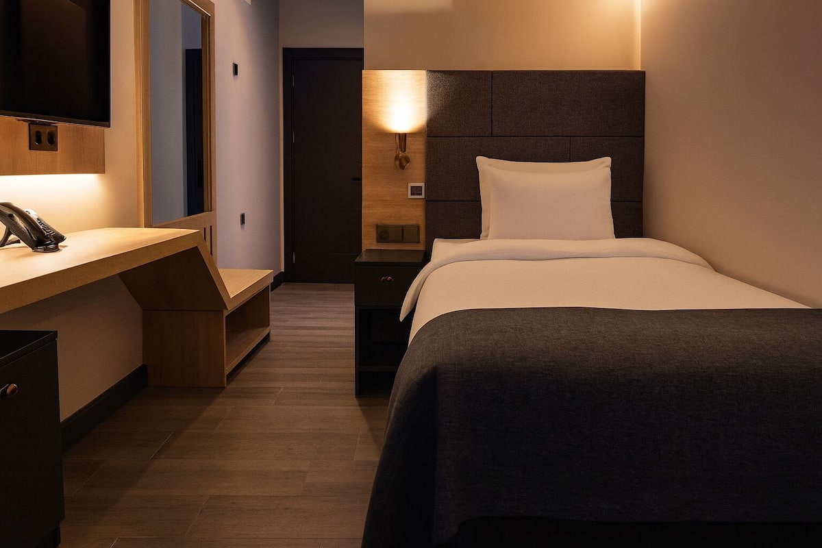 Ein Hotelzimmer mit Bett, Nachttisch, Lampe und einem an der Wand montierten Fernseher.