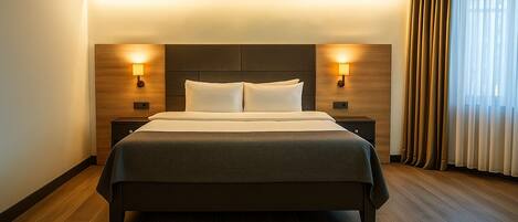 Habitación de hotel con una cama grande, dos lámparas de noche, cabecera de madera y una ventana con cortinas.