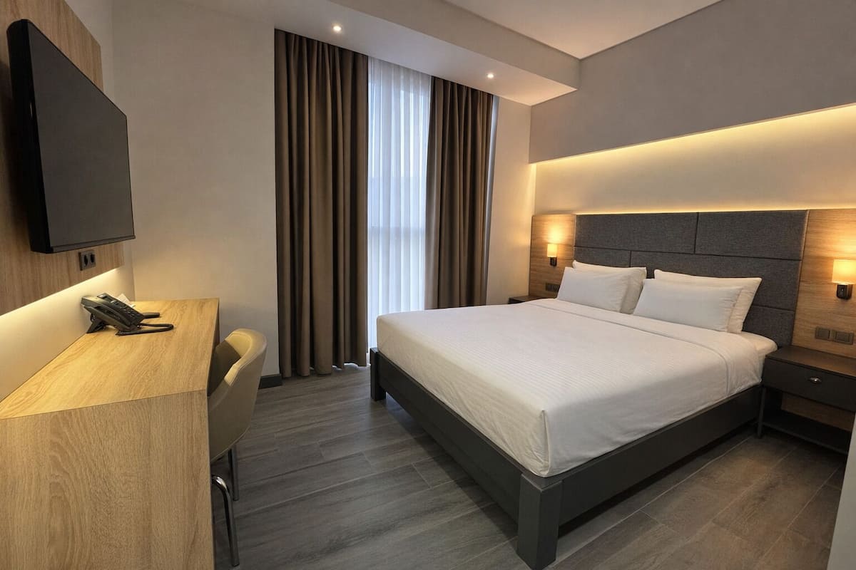 Ein modernes Hotelzimmer mit einem großen Bett, einem Schreibtisch mit Telefon und einem wandmontierten Flachbildfernseher.