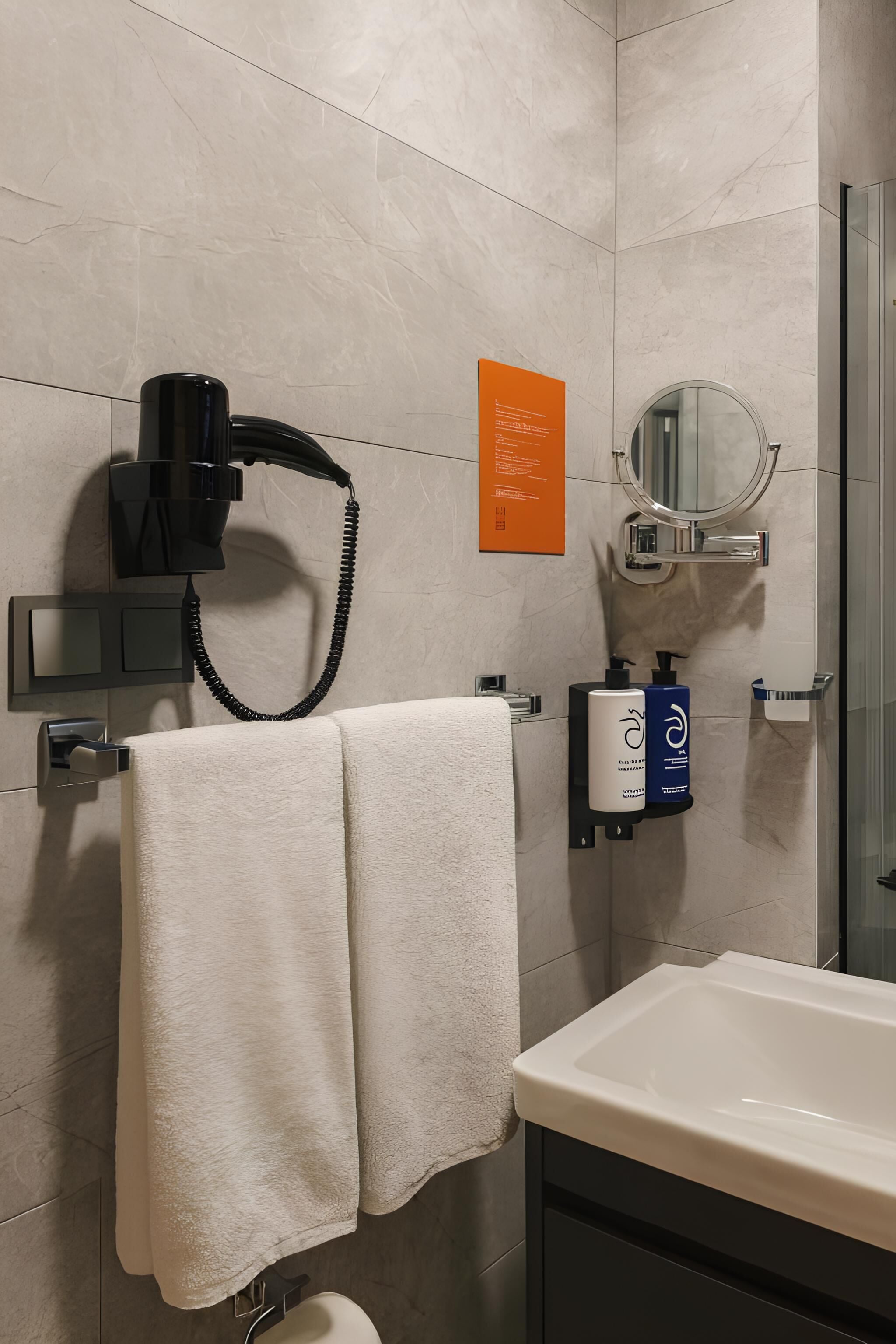 A modern bathroom with a hairdryer, towel rack, sink, and toiletries.