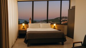 A hotel room with a large bed, two bedside tables with lamps, a view of a distant landscape through large windows, and a wardrobe. - Rest by Dedeman Sapanca (Sapanca)