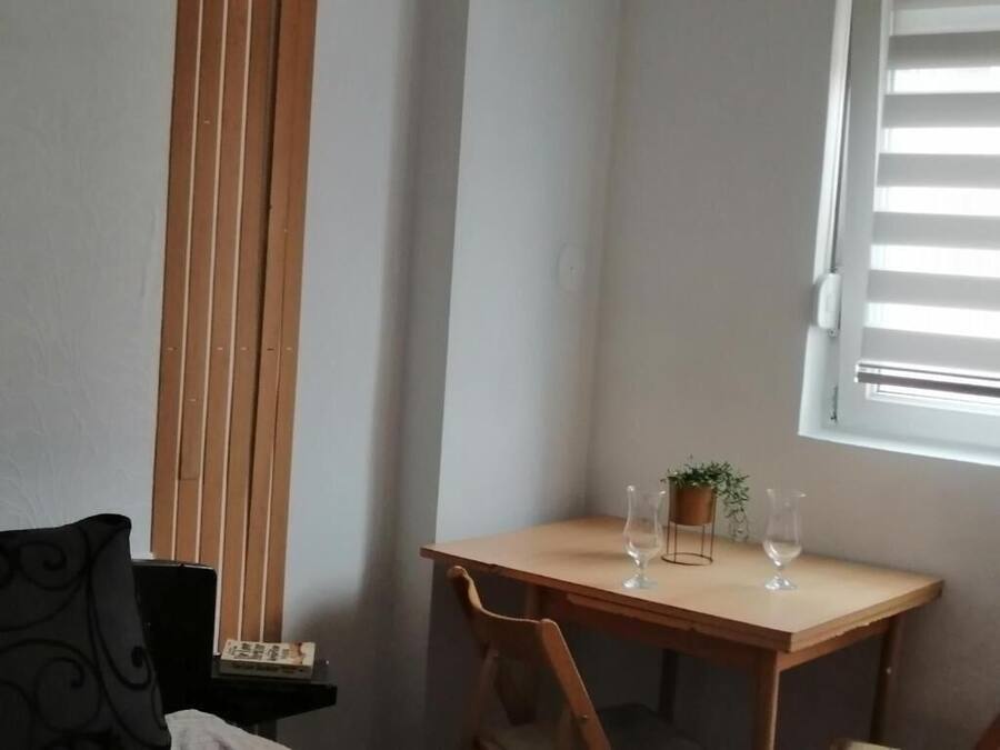 Una habitación pequeña y ordenada con una mesa de madera, dos sillas, una planta en maceta y una ventana con persianas.