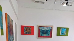 Eine Kunstgalerie mit einem beigen Sofa und einem Glastisch in der Mitte, umgeben von verschiedenen abstrakten Gemälden an den Wänden.