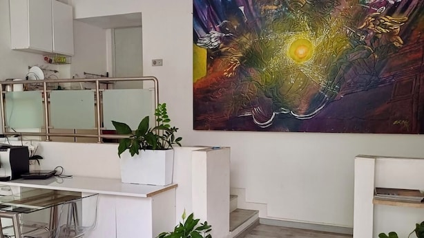 Eine moderne Küche mit weißen Schränken, einem Glastisch und einem großen abstrakten Gemälde an der Wand.
