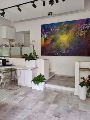A modern kitchen with white cabinetry, a glass dining table, and a large abstract painting on the wall. - Stay / Work / Meet – Creative Space in Centrum (Warsaw)