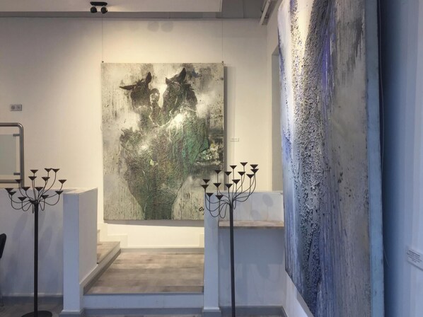 An art gallery with a large abstract painting on the wall and two black candelabras on pedestals.