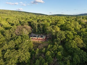 Vista aérea de una casa rodeada de un bosque denso, con un cielo despejado.