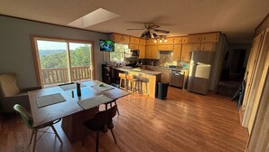 A kitchen with wooden cabinets, a dining table with chairs, a TV, and a ceiling fan. - A peaceful, forest retreat with stunning views near historic Harpers Ferry. (Harpers Ferry)