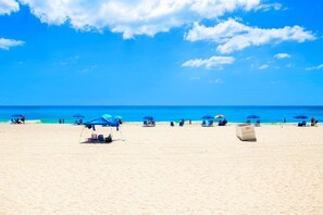 A beach with clear skies, blue umbrellas, and a few people.