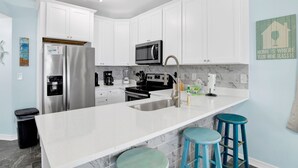 A modern kitchen with white cabinets, stainless steel appliances, a marble countertop, and blue bar stools. - Great Rates-Pet Friendly-Beachfront-Amazing View (Gulf Shores)