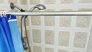A shower area with a blue shower curtain featuring a design, a handheld showerhead, and a tiled wall.