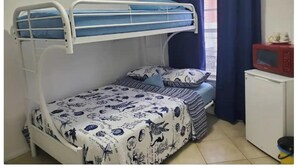 A bunk bed room with a lower bunk, a bed with patterned bedding, a microwave, and a small cabinet.