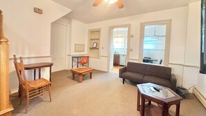 A spacious living room with a high ceiling fan, a wooden table, a sofa, and a chair. - 2 Bedroom Unit 5 Min to Walk GMC (Danville)
