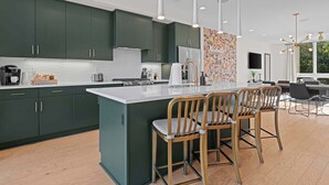A modern kitchen with dark green cabinets, a large island with bar stools, and a view of the outdoors through a window. - Artsy Luxe Nashville Stay |Rooftop Hot Tub & Views (Nashville)
