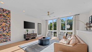 A modern living room with a sofa, a coffee table, a TV, and a large window with a view. - Artsy Luxe Nashville Stay |Rooftop Hot Tub & Views (Nashville)