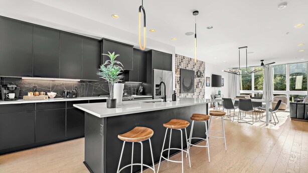 A modern kitchen with dark cabinetry, a marble backsplash, and a central island with bar stools.