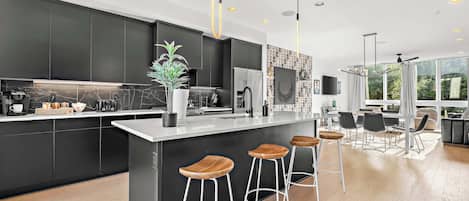 A modern kitchen with dark cabinetry, a marble backsplash, and a central island with bar stools.