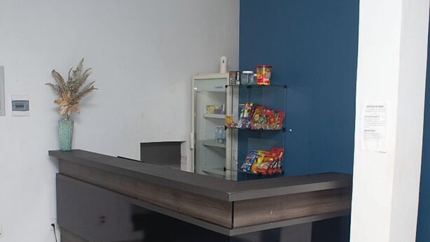 A reception desk with a dark wood finish, a glass display case with snacks, and a blue accent wall. - CBN HOTEL (Parauapebas)