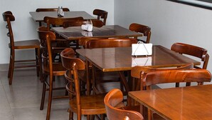 A hotel dining area with wooden tables and chairs, a white handbag on one table, and a logo for CBN Hotel in the bottom left corner. - CBN HOTEL (Parauapebas)