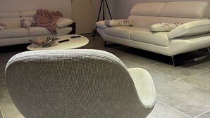Un salon moderne avec un canapé blanc, un fauteuil à motifs, une lampe sur pied et un tableau représentant un paysage urbain accroché au mur.