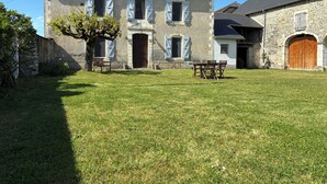 Une maison en pierre avec une grande porte d’entrée, une table à manger avec des chaises et une pelouse bien entretenue.