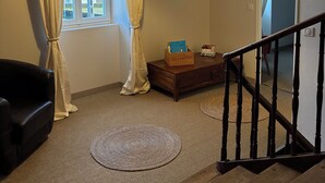 Une pièce avec un escalier en bois, une fenêtre avec des rideaux, un luminaire suspendu et une petite table en bois sur laquelle sont posés des livres.