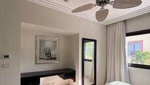 A hotel room with a bed, a ceiling fan, a window with curtains, a framed picture on the wall, and a small bathroom area.