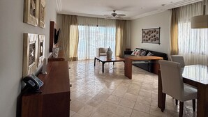 A spacious living room with a wooden desk, a sofa, a dining table with chairs, and a ceiling fan.