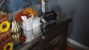 Una stanza con una scrivania, una lampada, un cesto e un quadro che raffigura un paesaggio urbano.