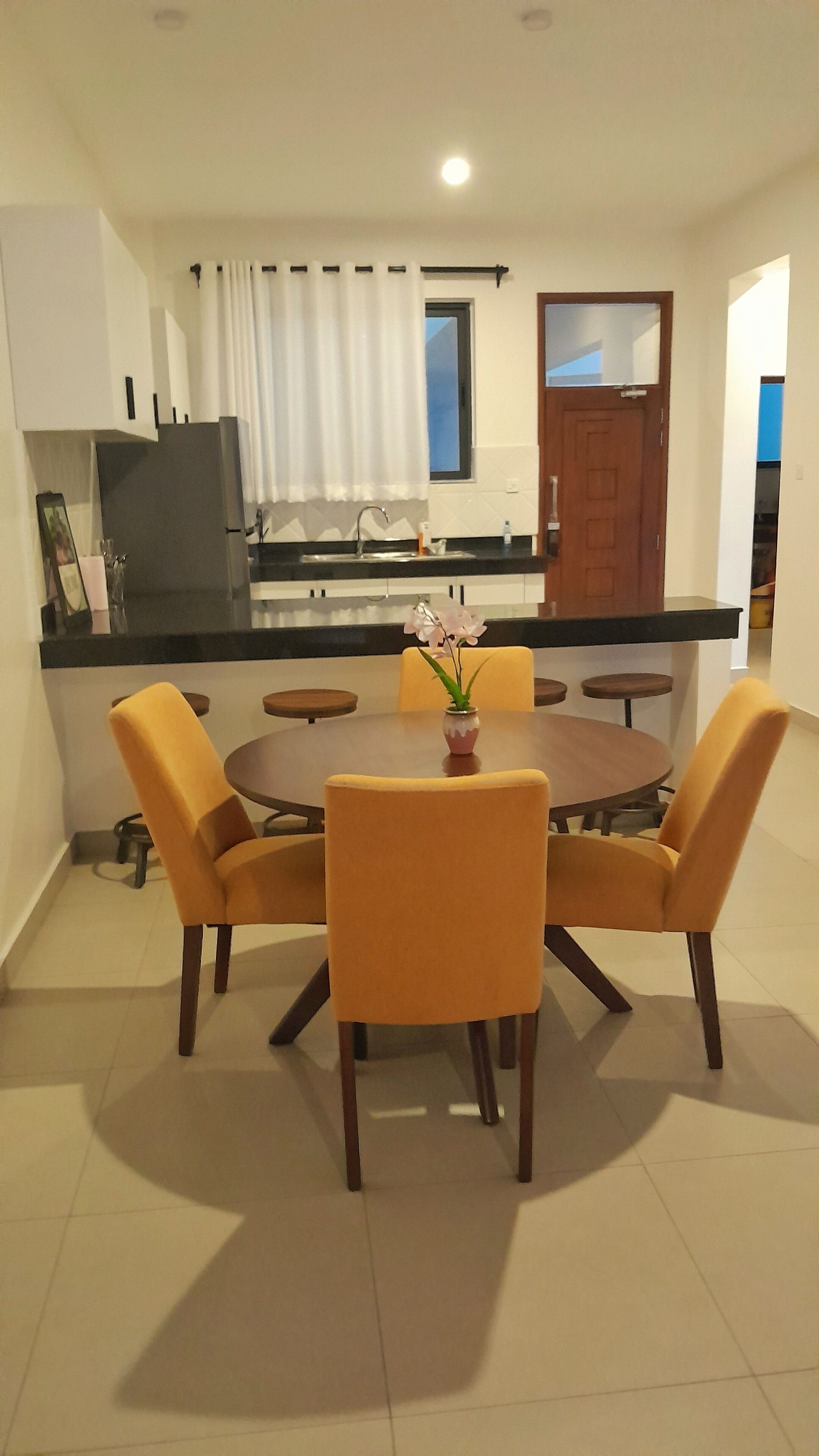 A dining area with a round table, six yellow chairs, and a vase with flowers.