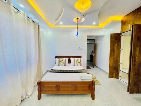 A bedroom with a wooden bed, white curtains, a ceiling fan, and a door leading to another room.
