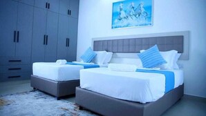 A modern hotel room with two beds, grey cabinets, a large painting, and a grey headboard. - Nyali Beachfront Apartments Baobab waves (Mombasa)