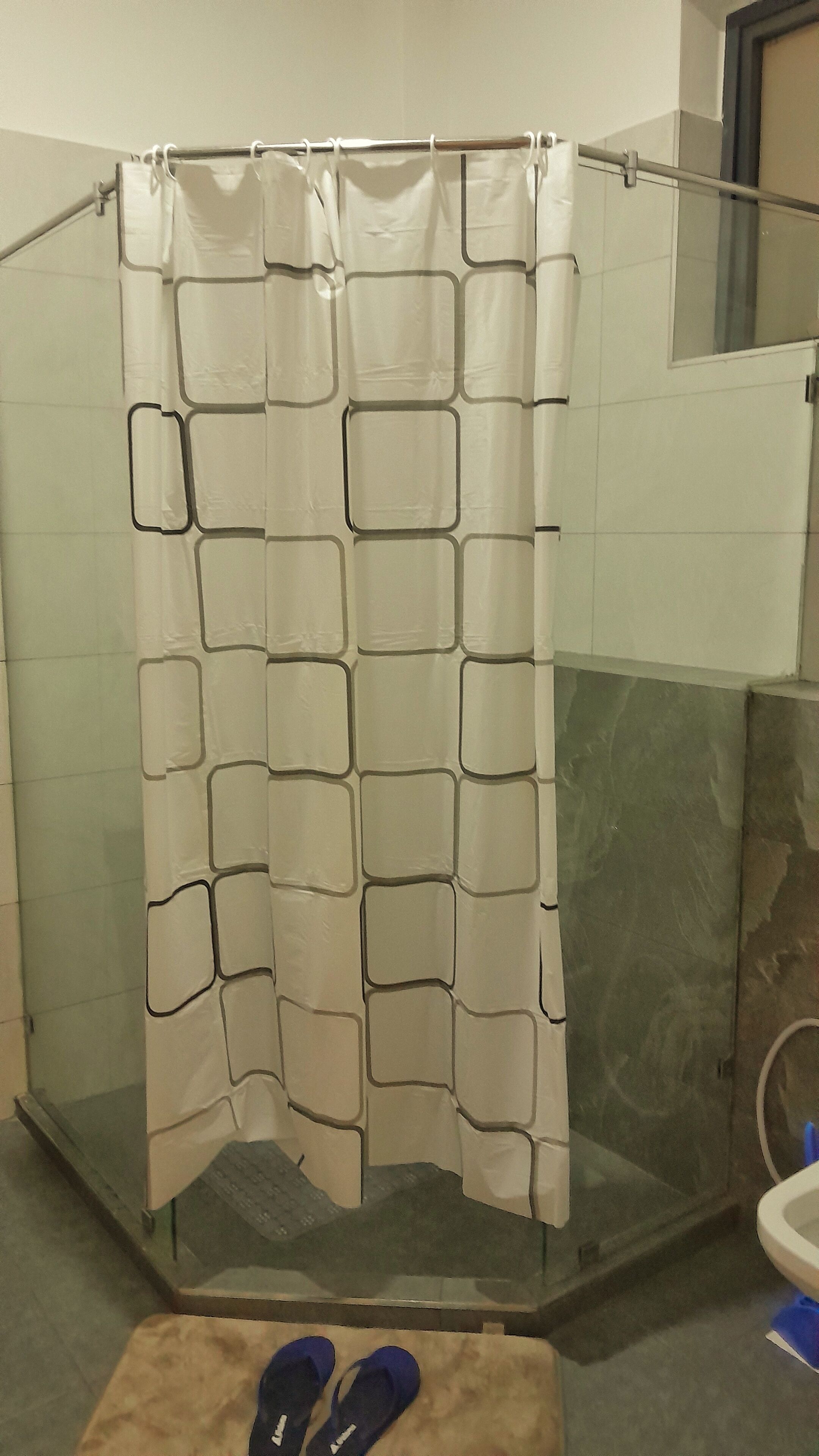 Ducha con cortina de estampado geométrico, puerta de cristal y un taburete pequeño con zapatillas.