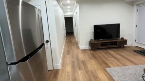 Un couloir avec un réfrigérateur en acier inoxydable, un meuble de rangement en bois intégrant un téléviseur et un plancher en bois.