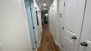 Un couloir étroit avec un plancher en bois, des murs blancs et des portes de chaque côté.