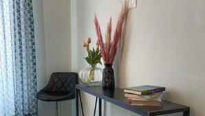 Eine Ecke eines Raumes mit einem schwarzen Stuhl, einem kleinen Tisch mit einer Vase und Büchern sowie einer Wandsteckdose.