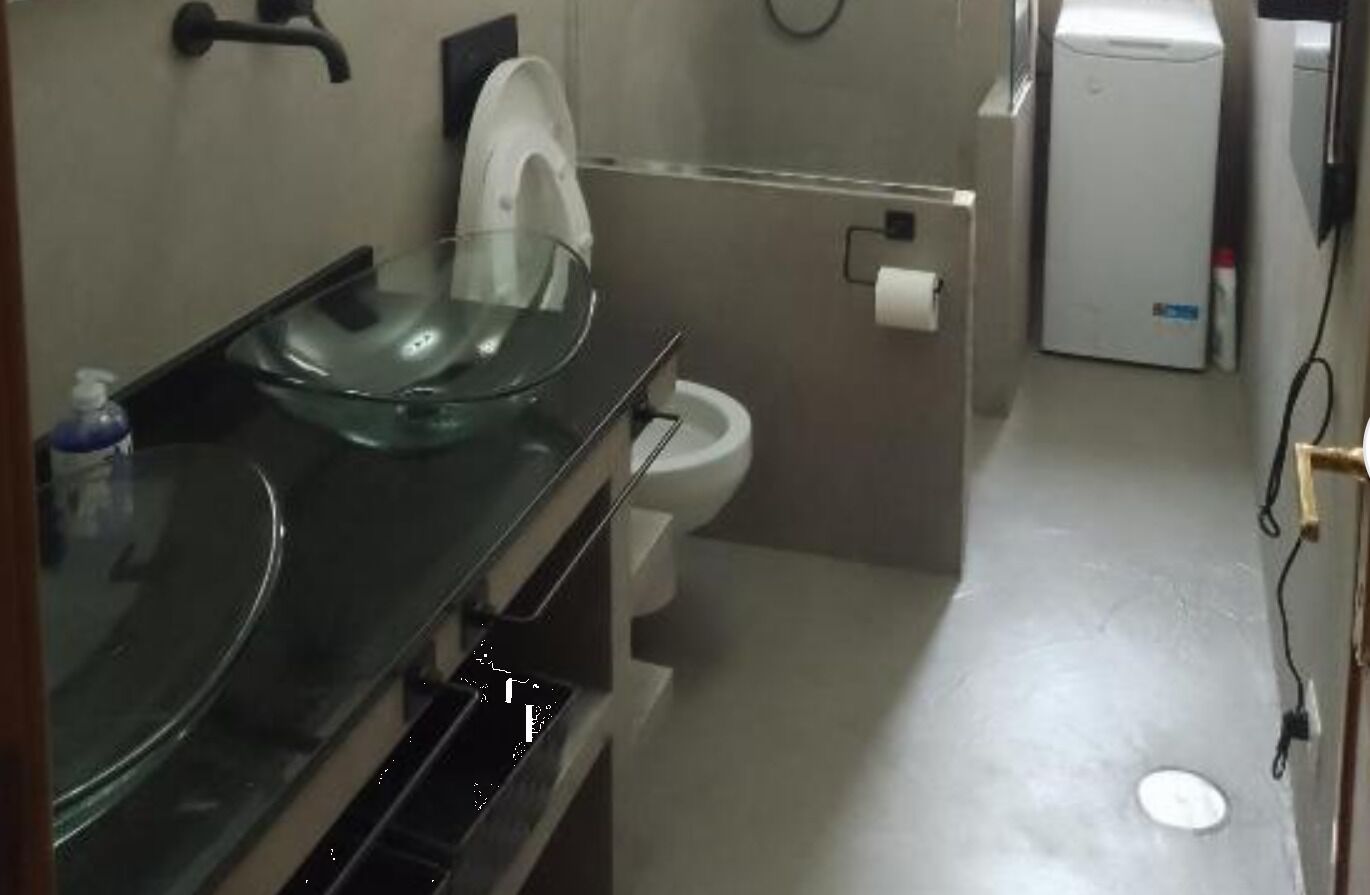 A bathroom with a glass sink, a toilet, and a small white appliance, possibly a heater or air purifier.