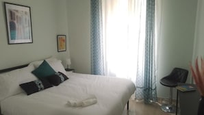 Ein Hotelzimmer mit einem großen Bett, einem Sessel, einem kleinen Tisch und einem Fenster mit Vorhängen.