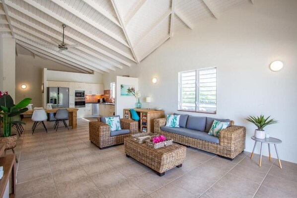 A spacious living area with wicker furniture, a dining table, and a kitchen in the background.