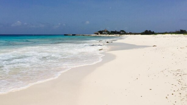 Ein Strand mit klarem türkisblauem Wasser, einem Sandstrand und einem Gebäude in der Ferne.