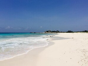 A beach with clear turquoise water, a sandy shore, and a building in the distance.