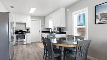Une cuisine moderne avec des meubles blancs, des appareils en acier inoxydable et un coin repas comprenant une table et des chaises en verre.