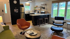 Et moderne køkken med en central ø, et spiseområde med et rundt bord og en opholdsstue med sofa og stole.