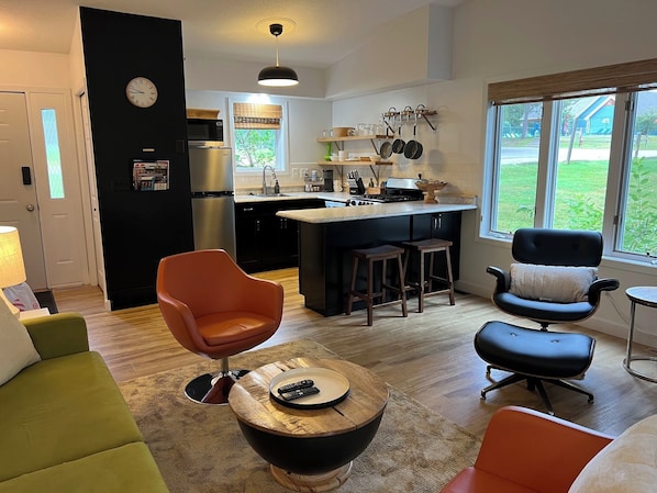 A modern kitchen with a central island, a dining area with a round table, and a living room with a sofa and chairs.