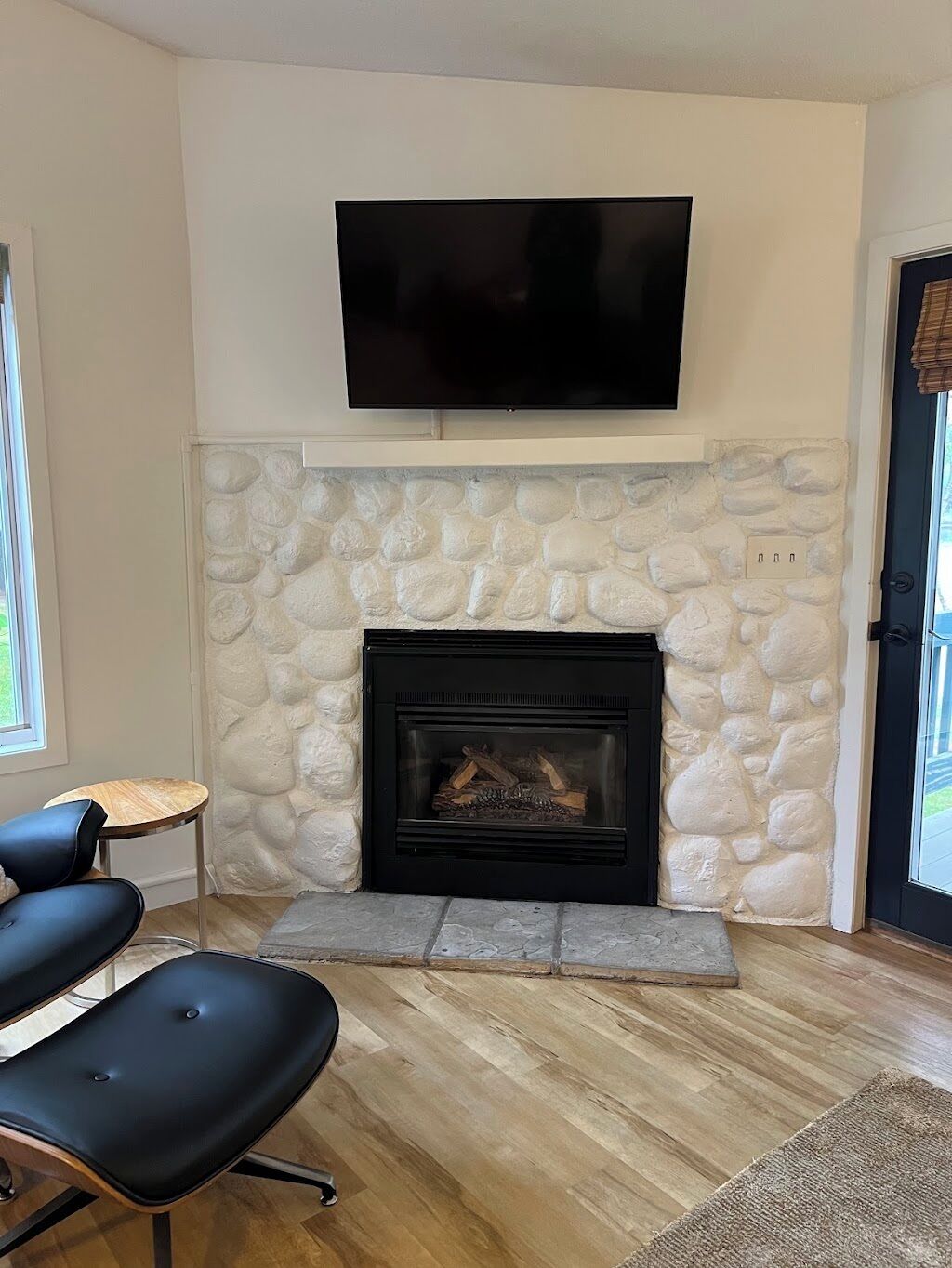 Un salón con chimenea de piedra, un televisor de pantalla plana montado encima y dos sillas negras.