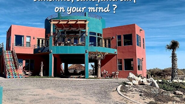 A colorful building with a staircase, a covered outdoor area, and a palm tree.
