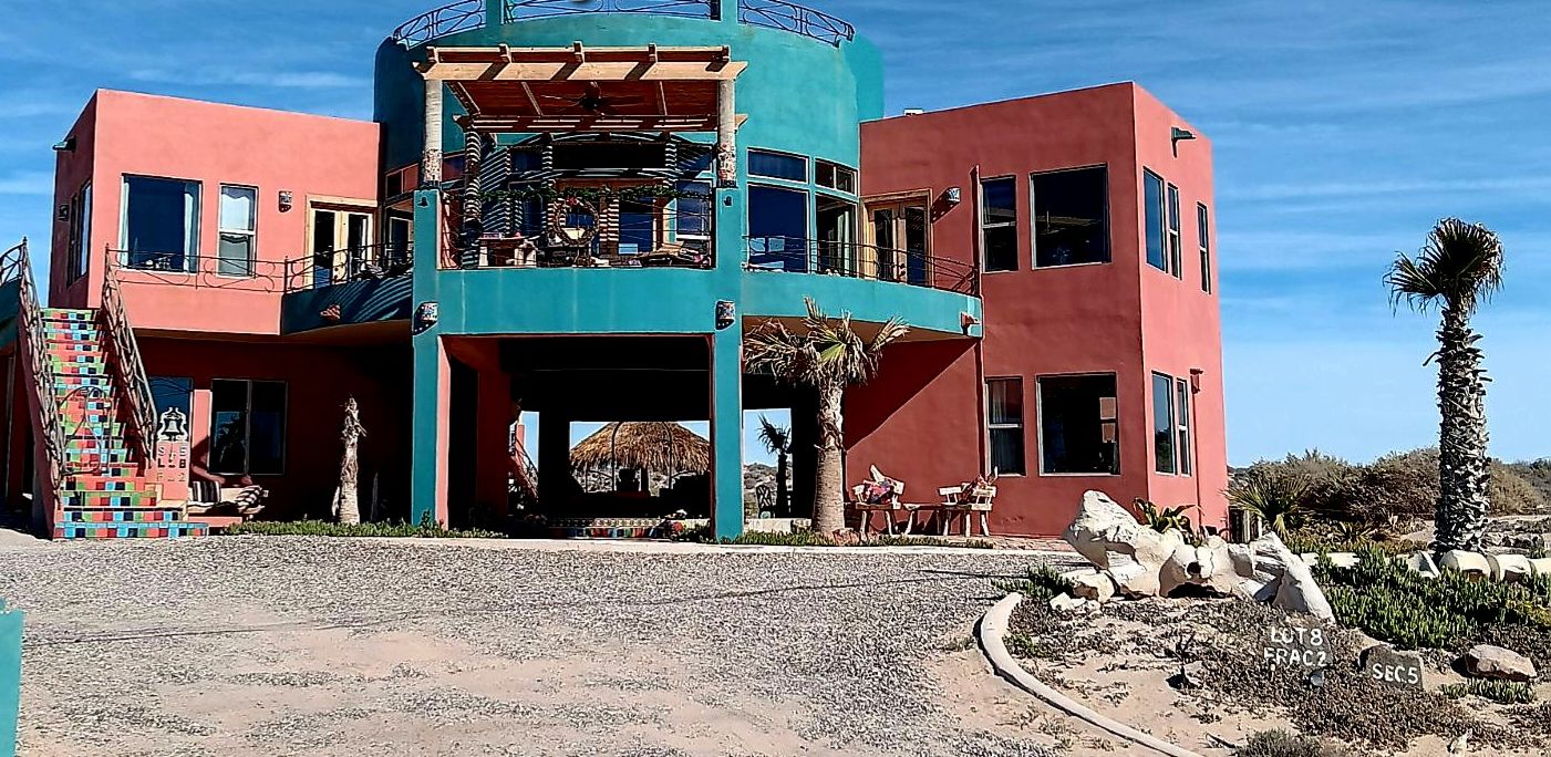 A colorful building with a staircase, a covered outdoor area, and a palm tree.
